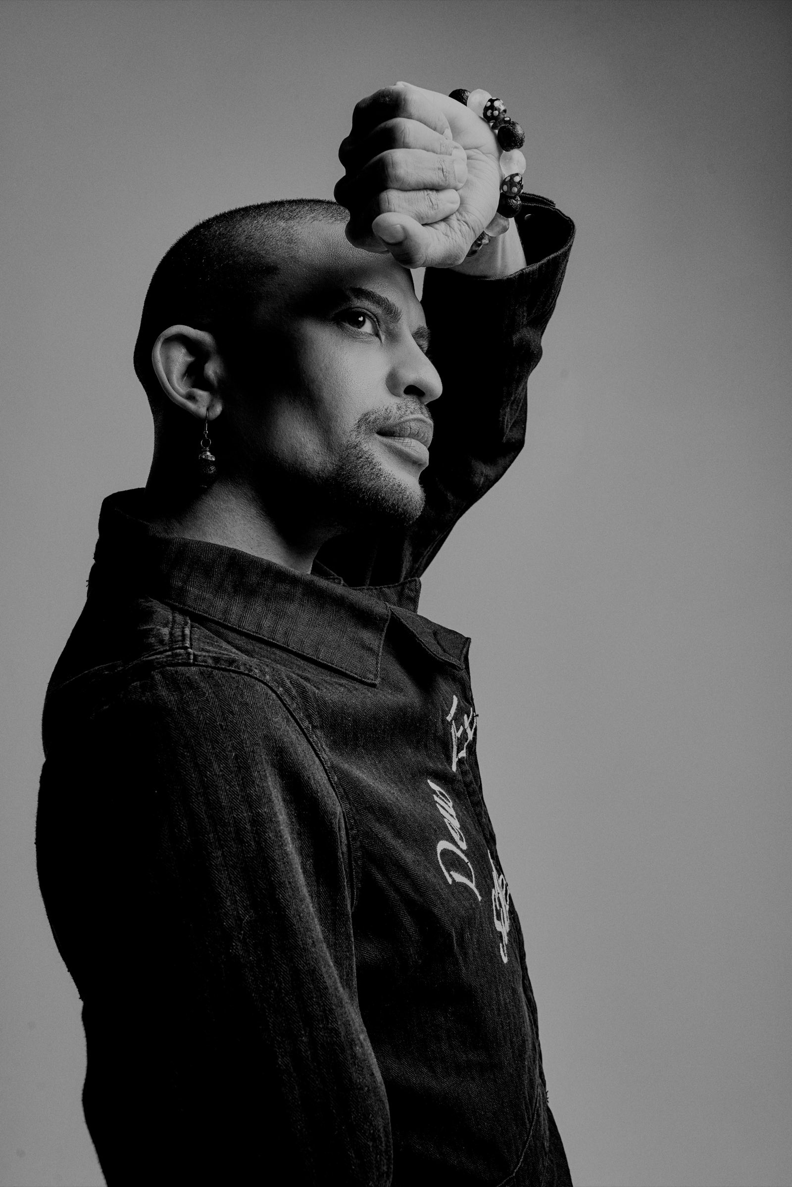 Traidy Naidoo in black and white, in profile with a fist raised to his brow.