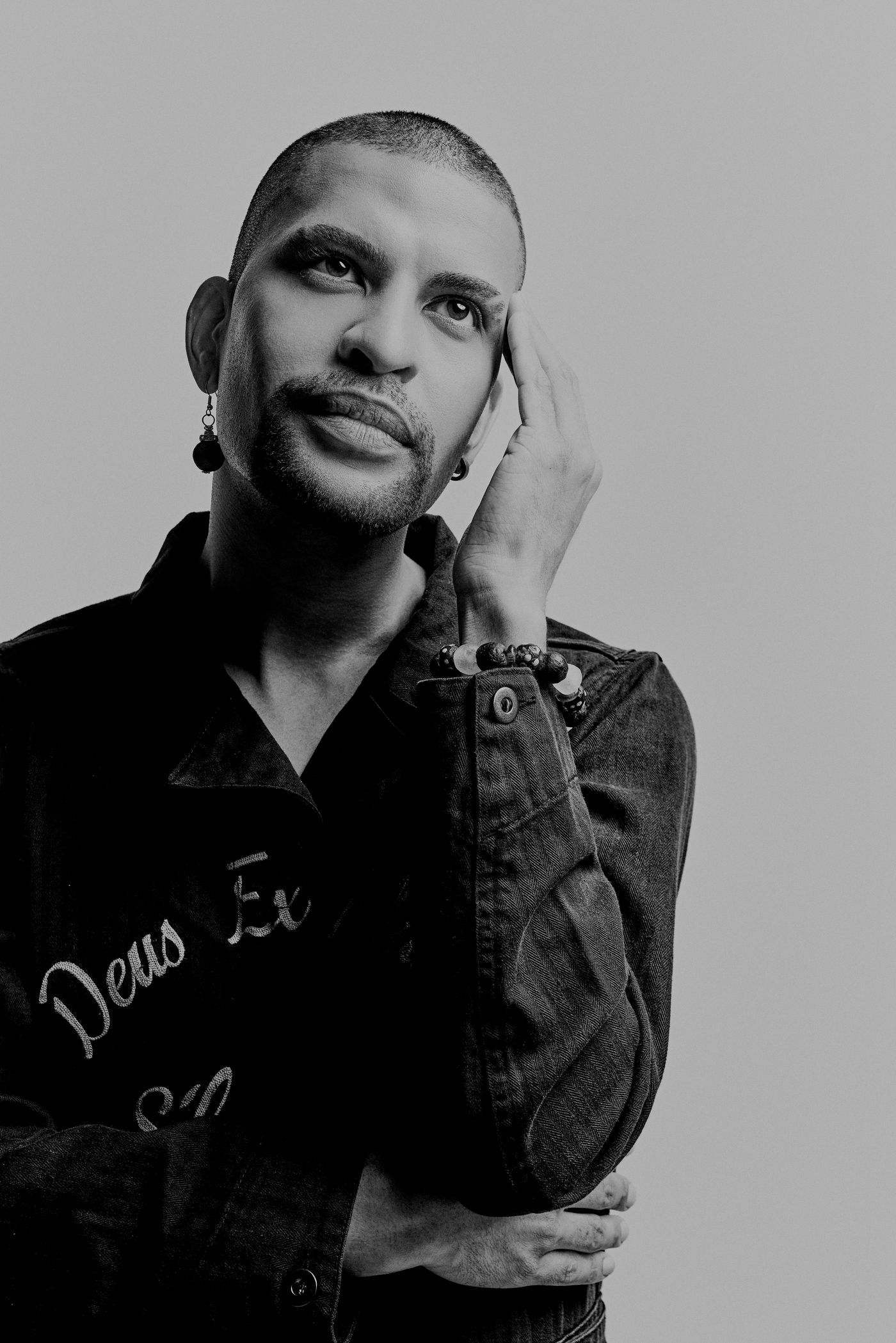 Traidy Naidoo in black and white, hand at his temple, looking down.