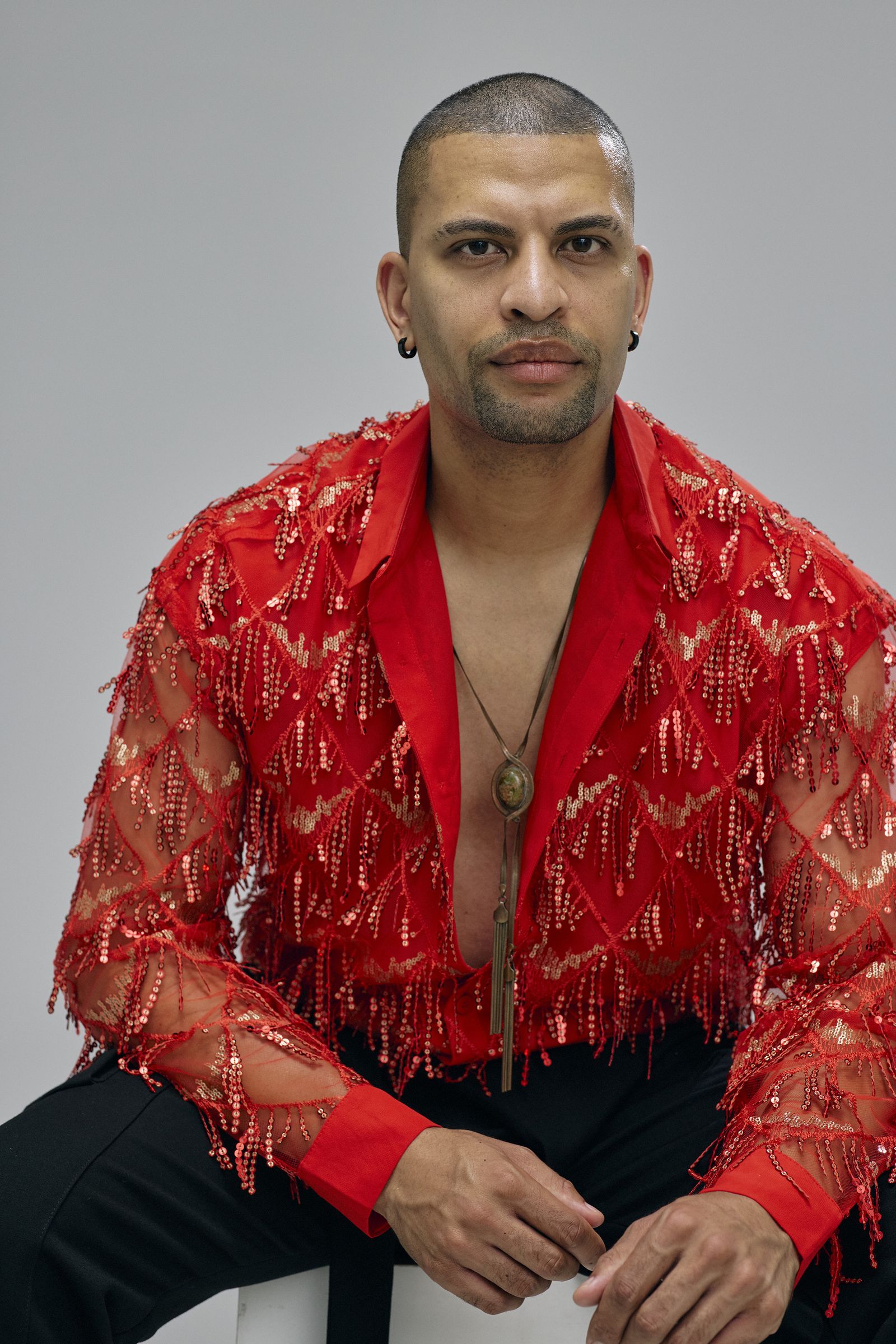 Traidy Naidoo in a red sequinned jacket against a red backdrop.