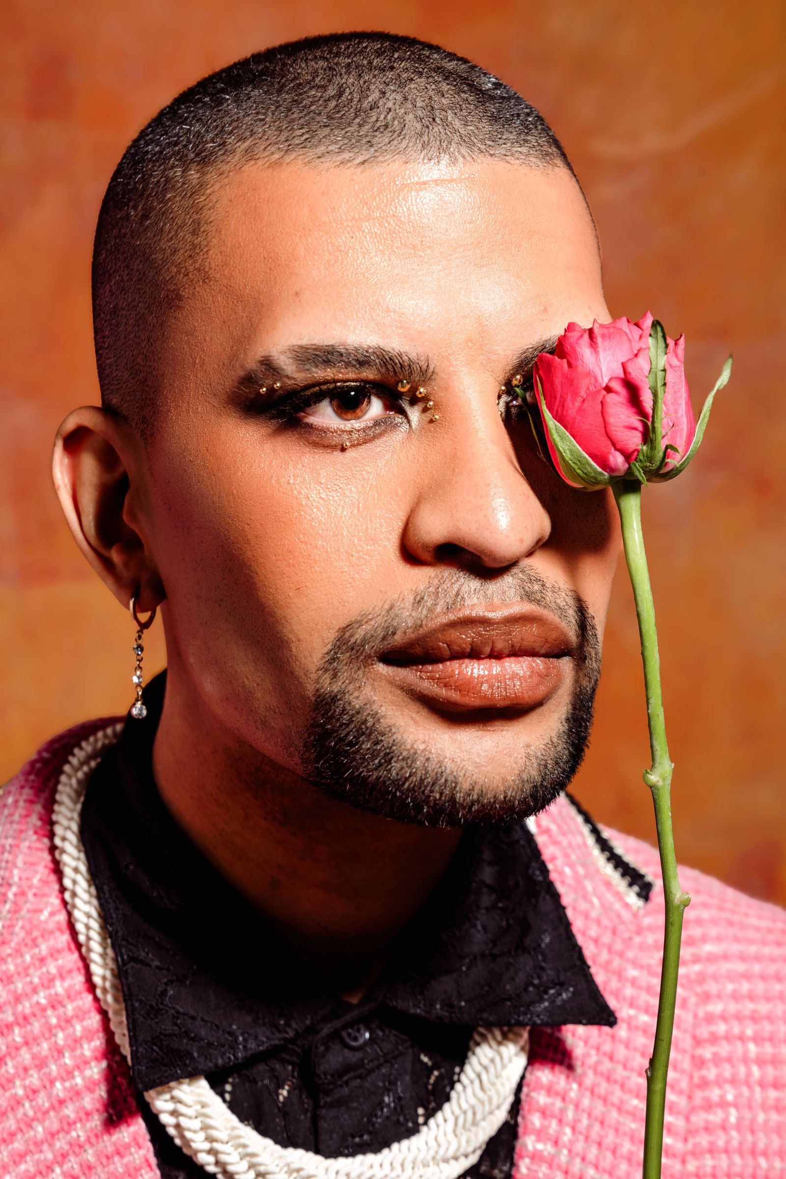 Traidy Naidoo in close-up holding a pink rose to his face.